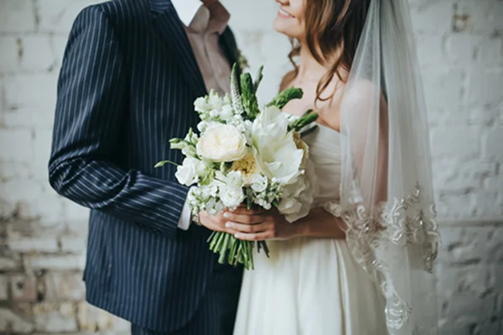 Photo d'un homme en costume et d'une femme en robe blanche de mariée. Ils se tiennent par la main en tenant un bouquet de fleurs blanches